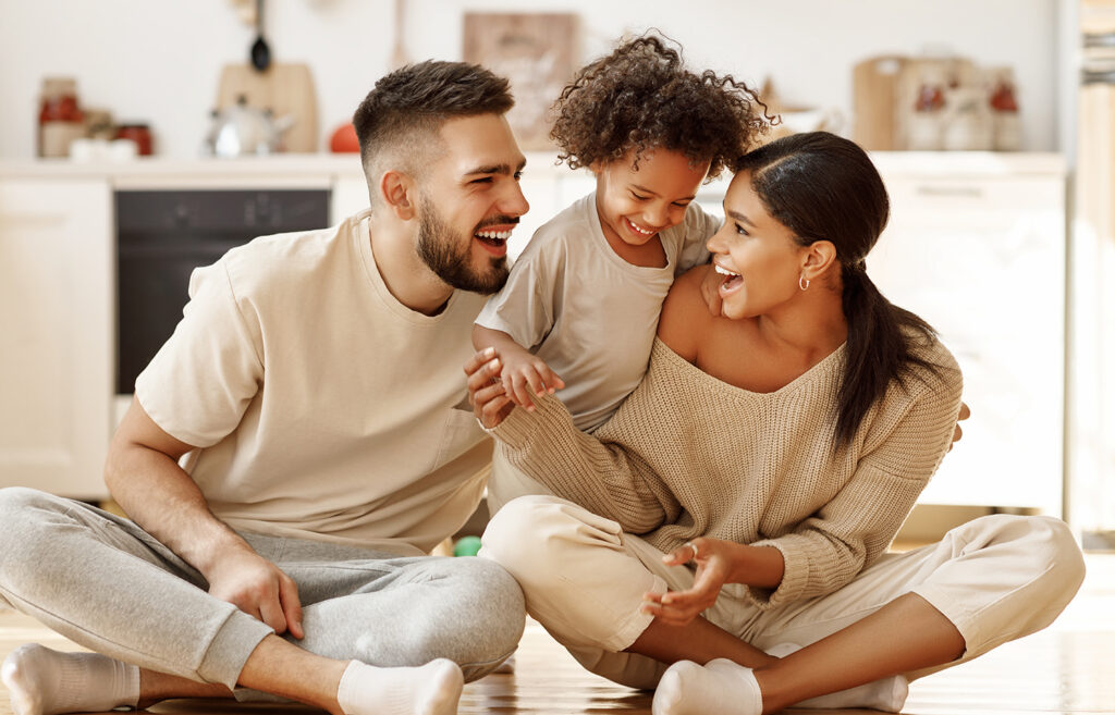 Happy Multiethnic Family Mom, Dad And Child Laughing, Playing And Tickles On Floor In Cozy Kitchen At Home